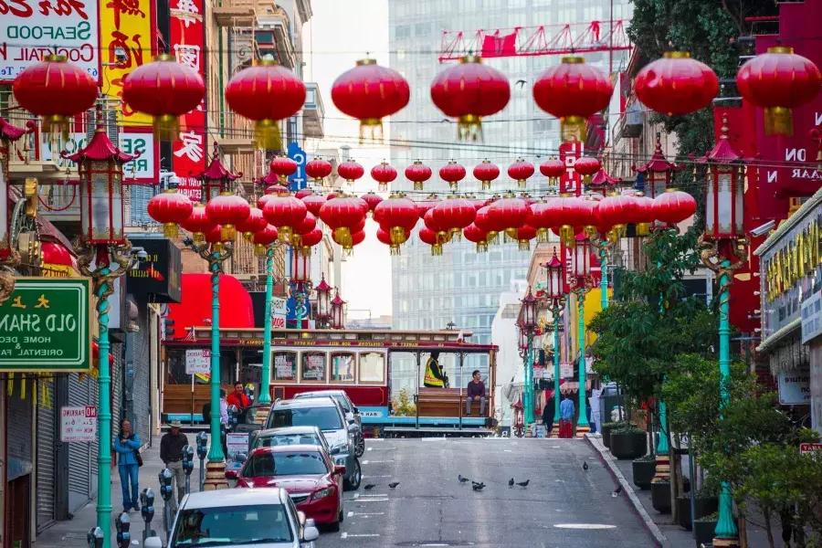 Uma rua montanhosa na 唐人街 de 贝博体彩app é retratada com lanternas vermelhas penduradas e um bonde passando.
