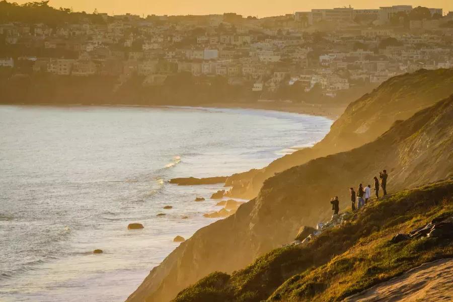 A group of people st和 on an oceanfront cliffside watching the sunset in San Francisco's Presidio.