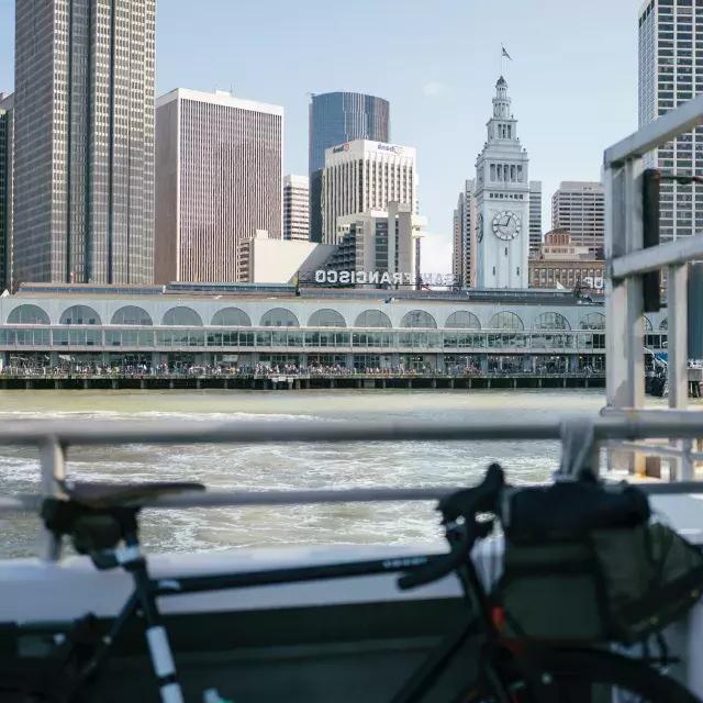 Bicicleta apoyada en una barandilla con el Ferry Building al fondo.
